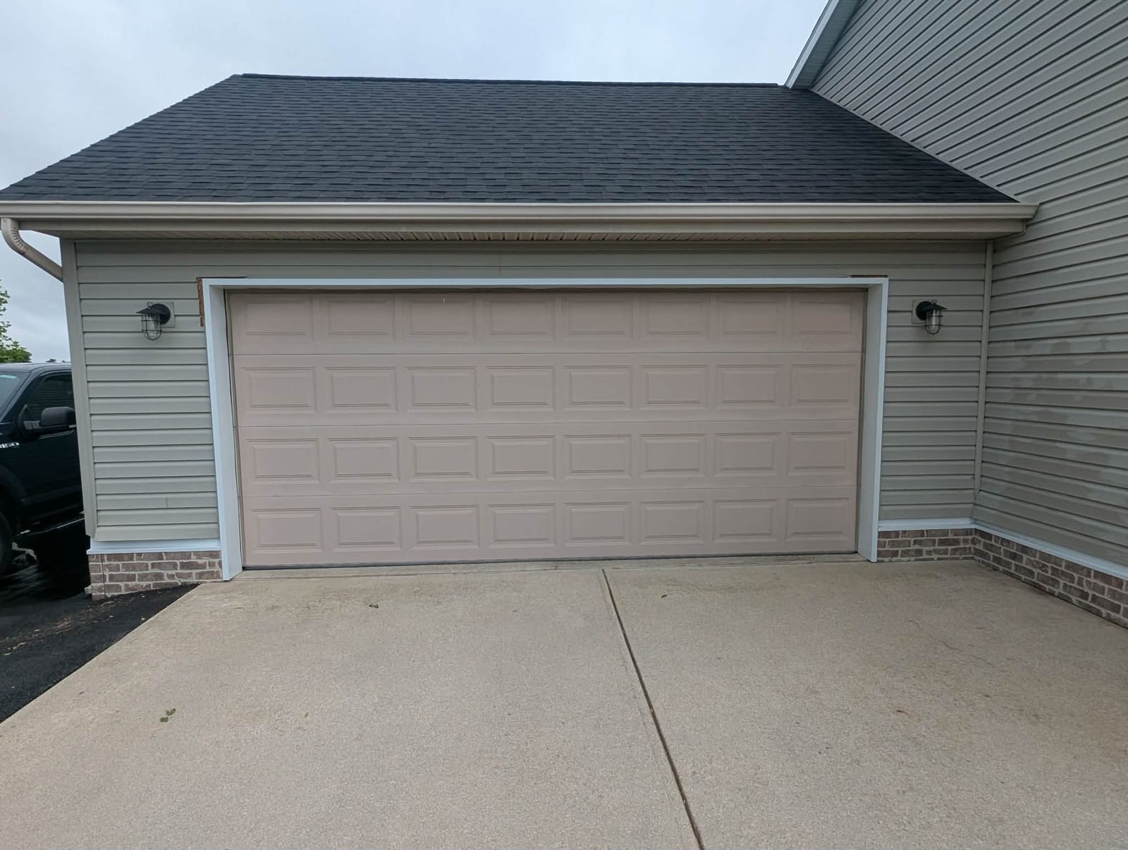 Dated almond raised-panel garage door on a gray-sided garage before replacement